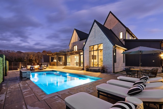 pool at dusk with outdoor lounge area and a patio area