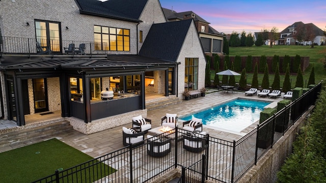 back house at dusk featuring an outdoor hangout area, a fenced in pool, a patio area, and a balcony