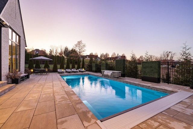 pool at dusk featuring pool water feature, a patio, and a hot tub