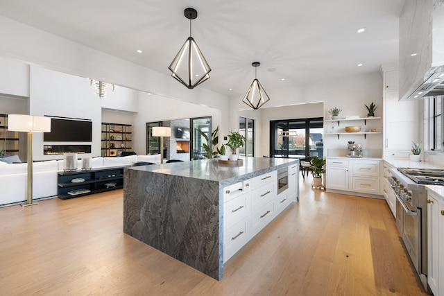 kitchen featuring pendant lighting, dark stone countertops, a large island, light hardwood / wood-style floors, and white cabinetry