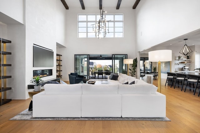 living room with beamed ceiling, a high ceiling, and light wood-type flooring