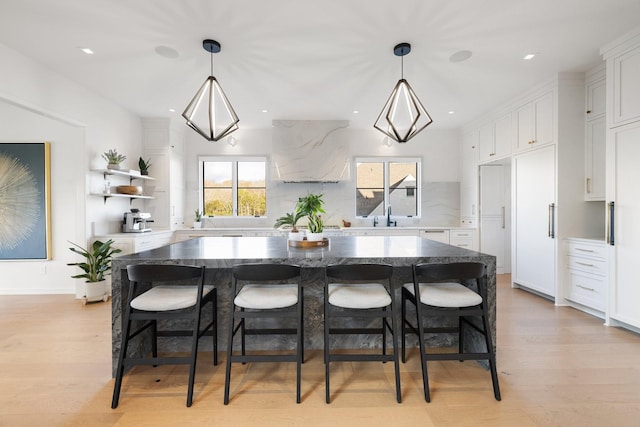 kitchen with a center island, white cabinets, hanging light fixtures, light hardwood / wood-style flooring, and light stone countertops