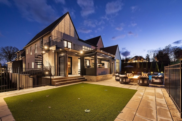 back house at dusk featuring a balcony, an outdoor fire pit, and a patio area