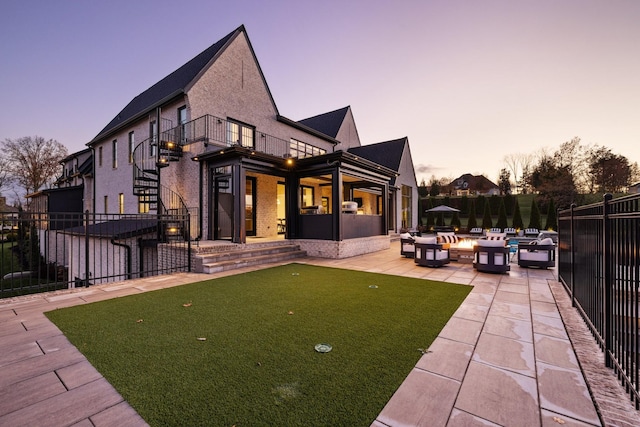 back house at dusk featuring a fire pit, a patio area, and a balcony