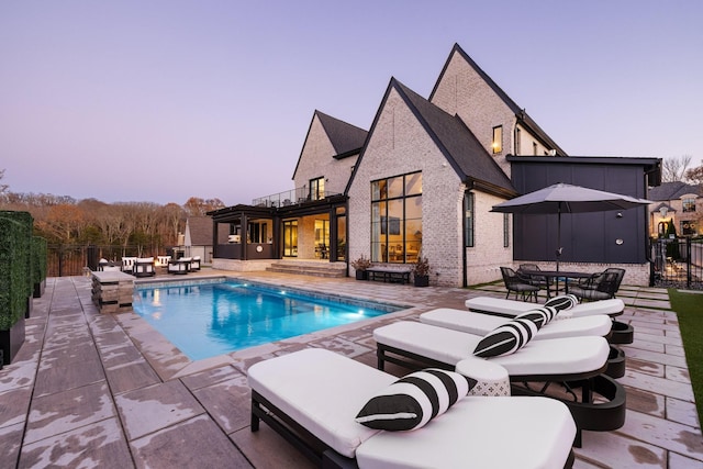 pool at dusk with outdoor lounge area and a patio