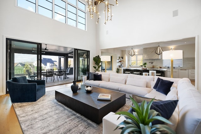 living room with light wood-type flooring, a towering ceiling, and ceiling fan with notable chandelier