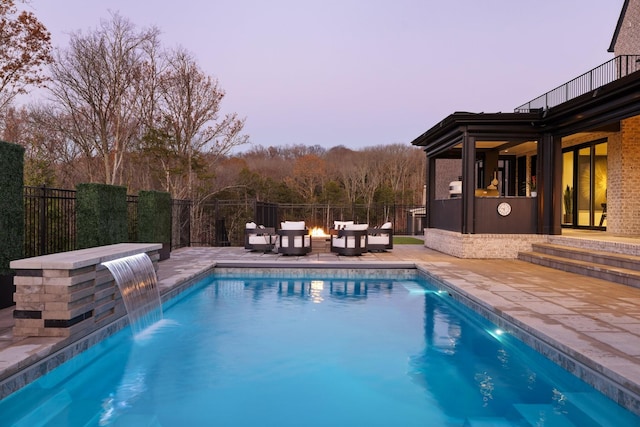 pool at dusk with a patio area and pool water feature