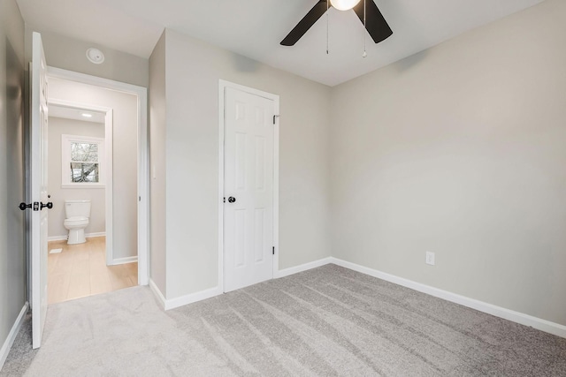 unfurnished bedroom featuring light carpet, a closet, ensuite bath, and ceiling fan