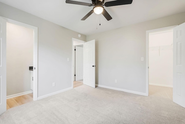 unfurnished bedroom featuring ceiling fan, light colored carpet, a walk in closet, and a closet