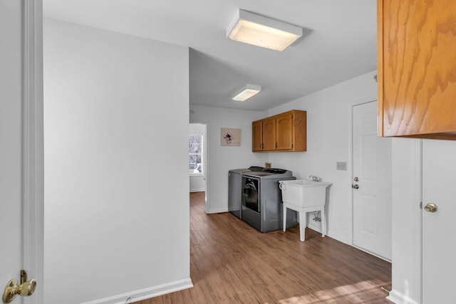 clothes washing area with washer and clothes dryer, cabinets, wood-type flooring, and sink