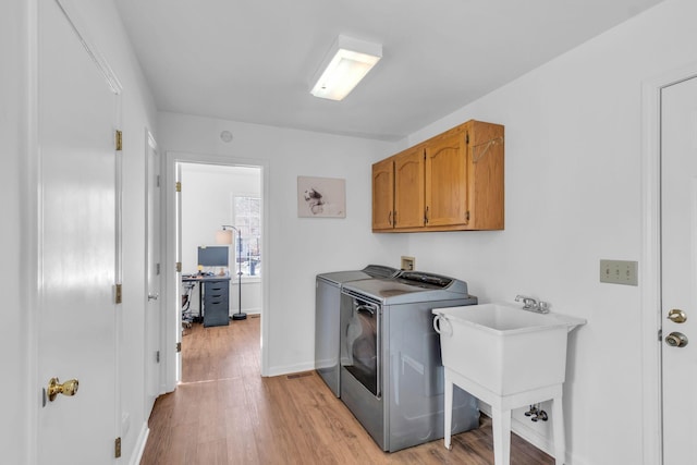 clothes washing area with washing machine and clothes dryer, light hardwood / wood-style flooring, cabinets, and sink