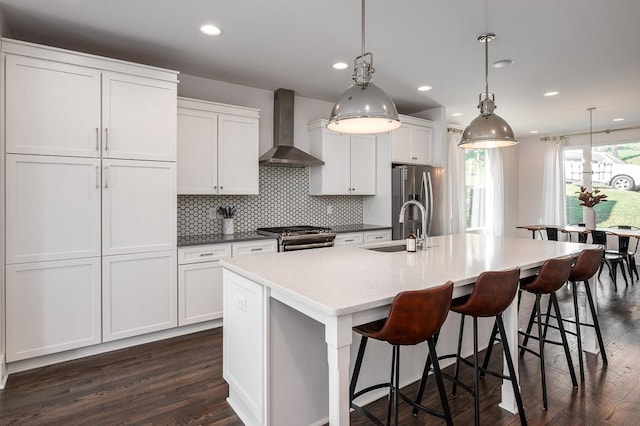 kitchen with dark hardwood / wood-style floors, a kitchen island with sink, stainless steel appliances, and wall chimney range hood