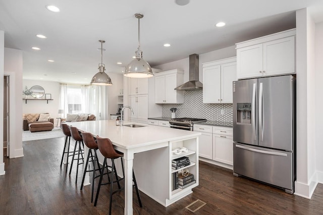 kitchen featuring sink, wall chimney exhaust hood, stainless steel appliances, a kitchen island with sink, and white cabinets