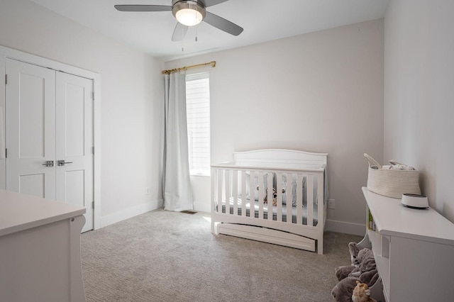 bedroom featuring ceiling fan, a closet, light colored carpet, and a crib