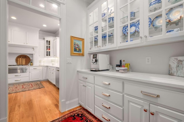 bar featuring stainless steel dishwasher, light hardwood / wood-style floors, white cabinetry, and crown molding