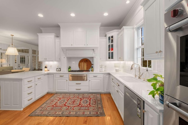 kitchen featuring white cabinetry, sink, stainless steel dishwasher, crown molding, and decorative light fixtures