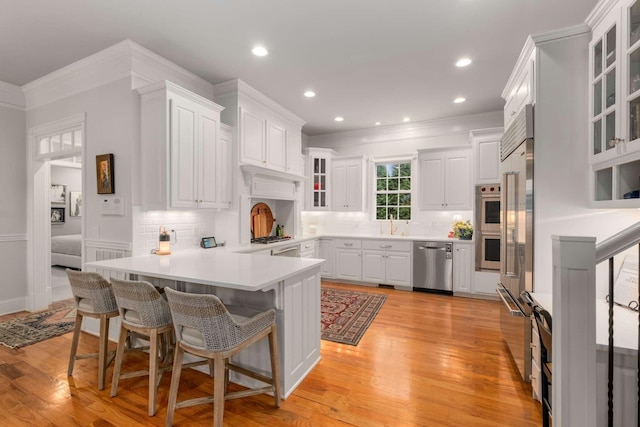 kitchen with stainless steel dishwasher, decorative backsplash, light hardwood / wood-style floors, white cabinetry, and a breakfast bar area