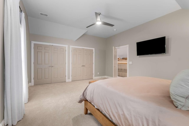 bedroom with ceiling fan, light carpet, and two closets