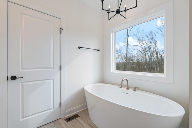 bathroom with hardwood / wood-style floors, a tub to relax in, and a chandelier