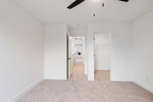 unfurnished bedroom featuring ceiling fan, light colored carpet, a walk in closet, and a closet