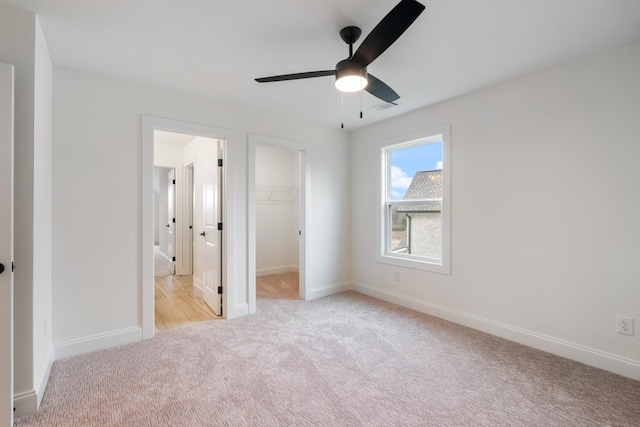 unfurnished bedroom with a walk in closet, ceiling fan, a closet, and light colored carpet