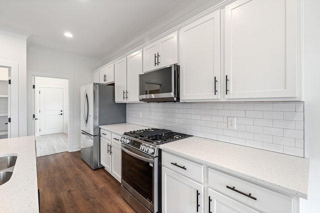 kitchen featuring appliances with stainless steel finishes, dark hardwood / wood-style flooring, light stone counters, ornamental molding, and white cabinets