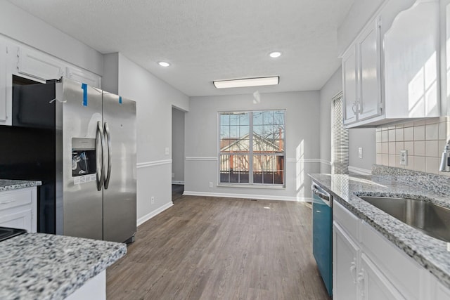 kitchen with backsplash, light stone counters, stainless steel appliances, hardwood / wood-style floors, and white cabinetry