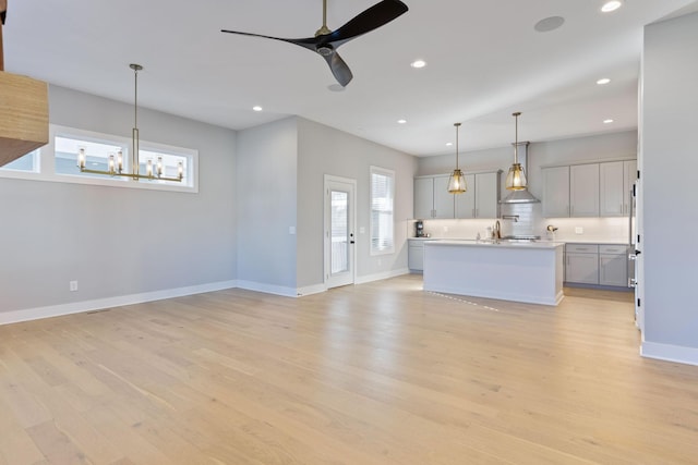 unfurnished living room with ceiling fan with notable chandelier, light hardwood / wood-style flooring, and sink