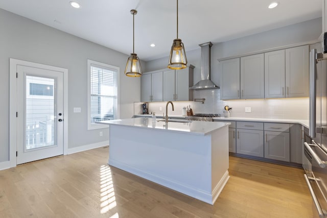 kitchen with tasteful backsplash, sink, wall chimney range hood, decorative light fixtures, and light hardwood / wood-style flooring