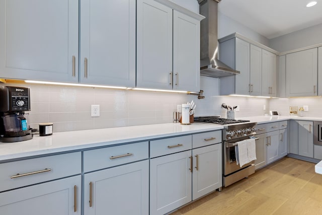 kitchen with decorative backsplash, high end stove, light hardwood / wood-style floors, and wall chimney range hood