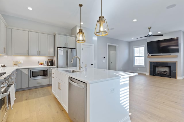 kitchen featuring a kitchen island with sink, hanging light fixtures, sink, light hardwood / wood-style flooring, and appliances with stainless steel finishes