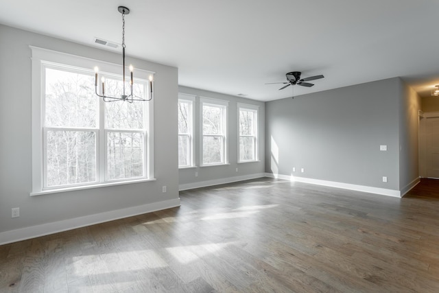 unfurnished dining area featuring ceiling fan with notable chandelier, a healthy amount of sunlight, and dark wood-type flooring