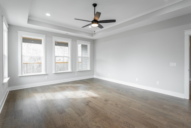 spare room with a raised ceiling, ceiling fan, and dark hardwood / wood-style flooring