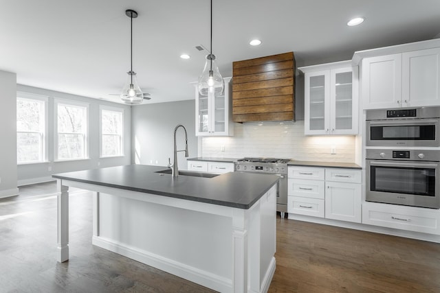 kitchen with premium range hood, appliances with stainless steel finishes, white cabinetry, sink, and a center island with sink