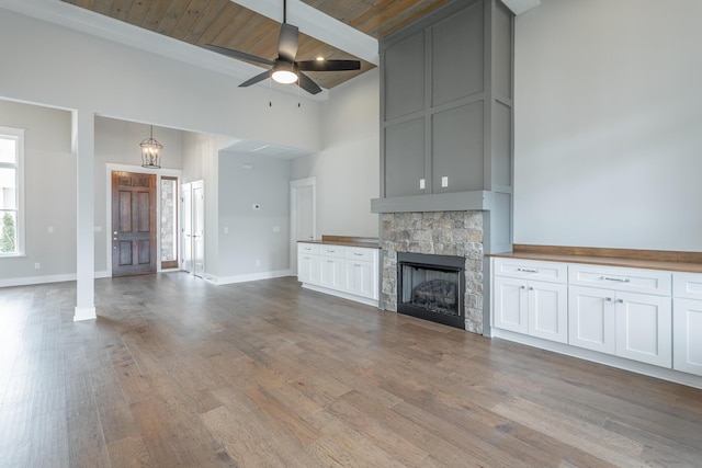 unfurnished living room with a stone fireplace, light hardwood / wood-style flooring, wooden ceiling, ceiling fan, and a high ceiling