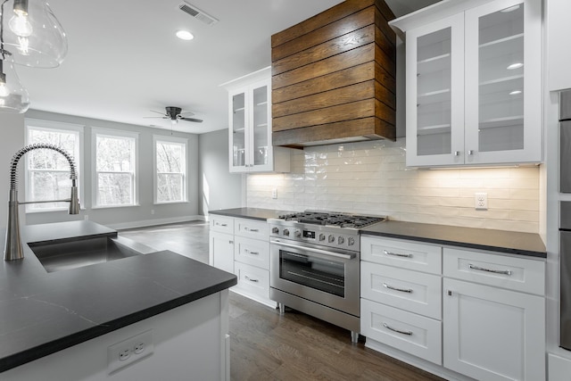 kitchen with pendant lighting, white cabinetry, sink, stainless steel gas range oven, and custom range hood