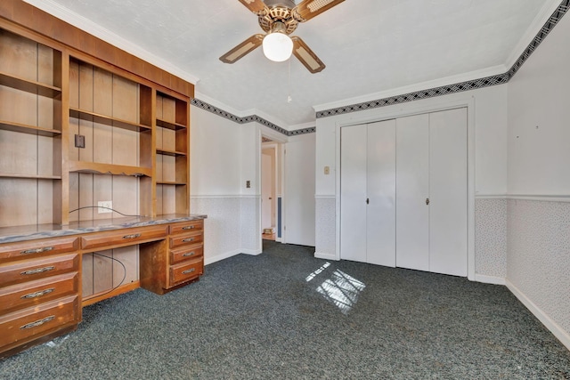 unfurnished office with built in desk, ceiling fan, ornamental molding, and dark carpet