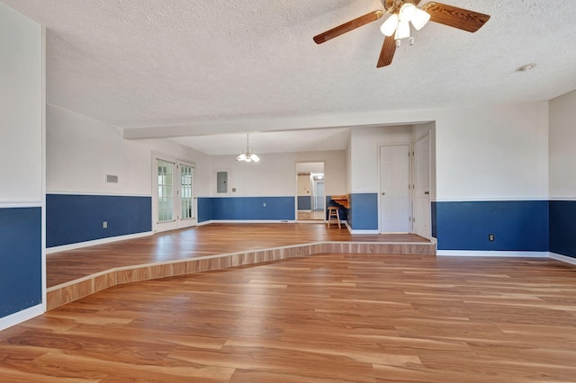 unfurnished living room featuring ceiling fan with notable chandelier, french doors, a textured ceiling, and light hardwood / wood-style floors