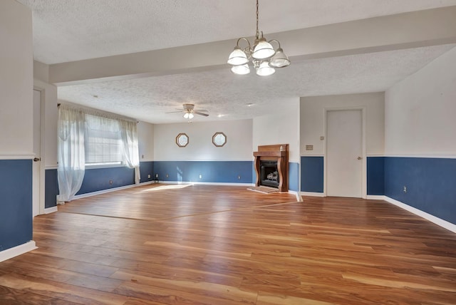 unfurnished living room with ceiling fan with notable chandelier, a textured ceiling, and hardwood / wood-style floors