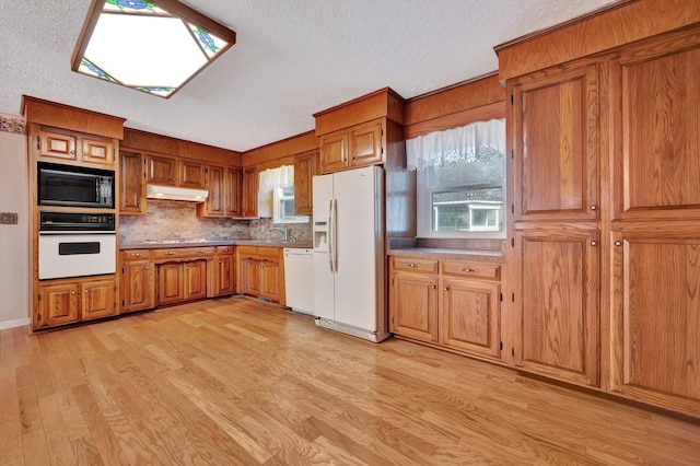 kitchen featuring white appliances, a textured ceiling, light wood-type flooring, and a wealth of natural light