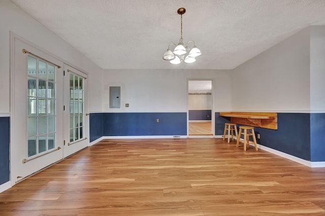 unfurnished dining area featuring electric panel, a notable chandelier, a textured ceiling, and light hardwood / wood-style floors