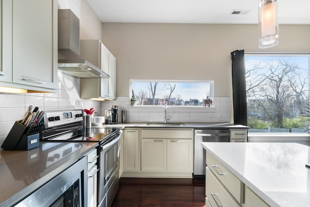 kitchen with backsplash, wall chimney range hood, sink, appliances with stainless steel finishes, and dark hardwood / wood-style flooring