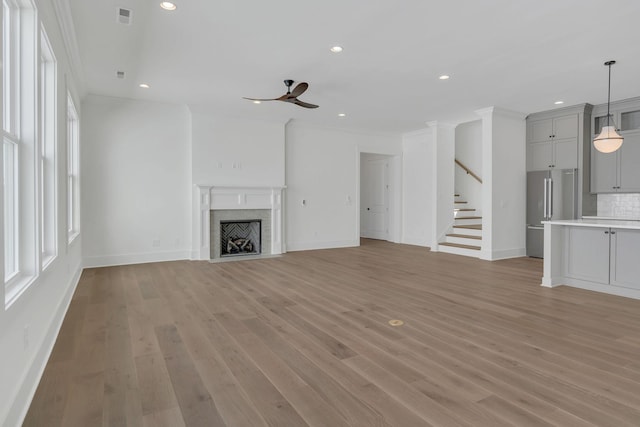 unfurnished living room with light wood finished floors, visible vents, a fireplace with flush hearth, ceiling fan, and crown molding