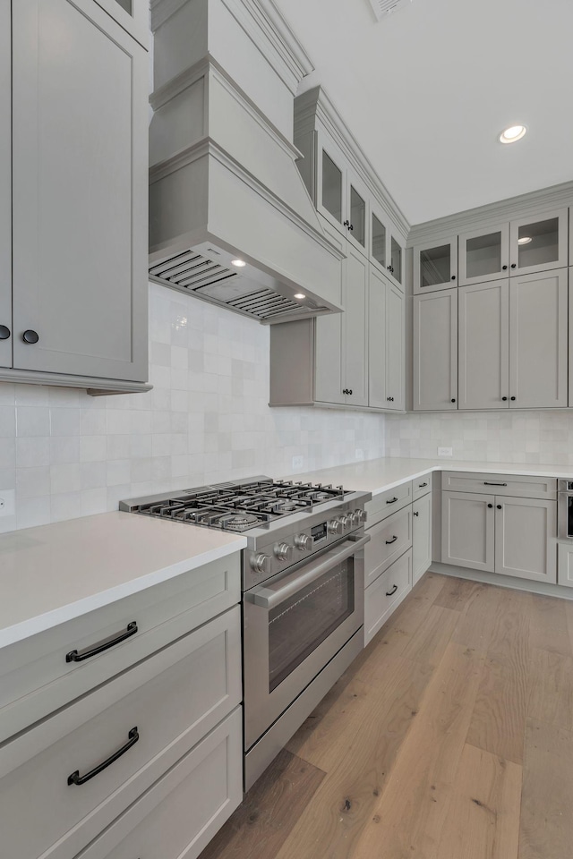 kitchen with light wood-style flooring, light countertops, high end stainless steel range, tasteful backsplash, and custom range hood