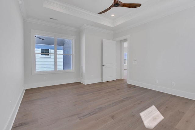 spare room featuring wood finished floors, visible vents, a ceiling fan, ornamental molding, and a tray ceiling