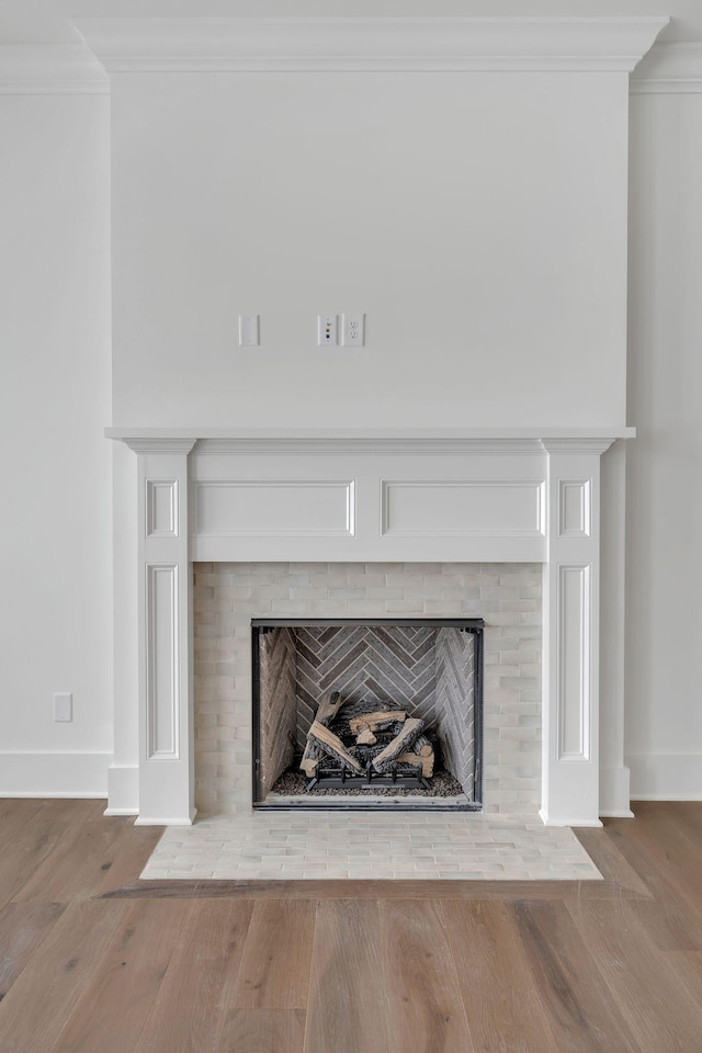 interior details featuring ornamental molding, a brick fireplace, and wood finished floors