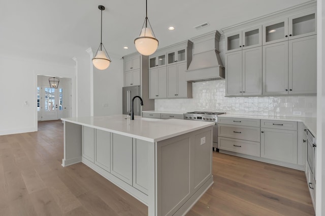 kitchen with a center island with sink, visible vents, a sink, high quality appliances, and premium range hood