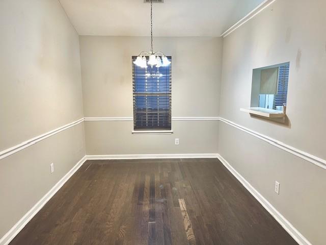 empty room featuring a notable chandelier and dark wood-type flooring