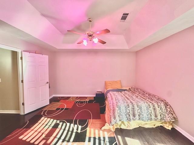 bedroom with hardwood / wood-style floors, a tray ceiling, and ceiling fan