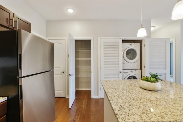 kitchen featuring stainless steel fridge, dark hardwood / wood-style flooring, light stone counters, pendant lighting, and stacked washer and dryer